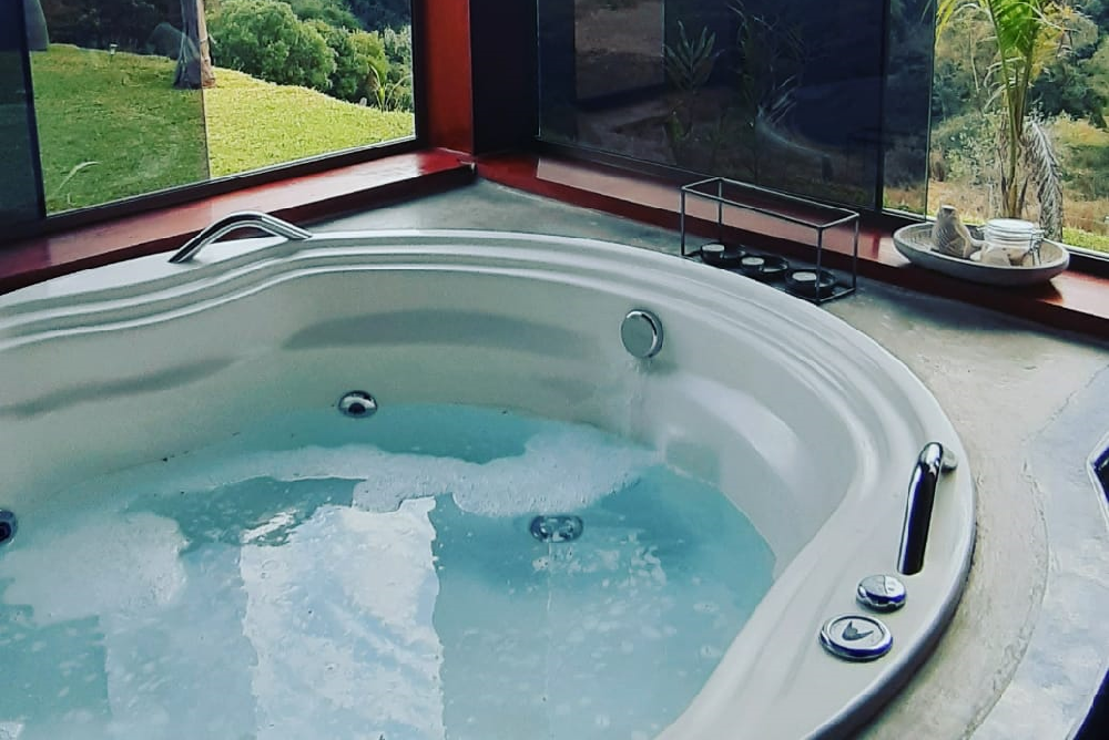 Spa montado em casa ao lado de uma janela que mostra uma área verde.